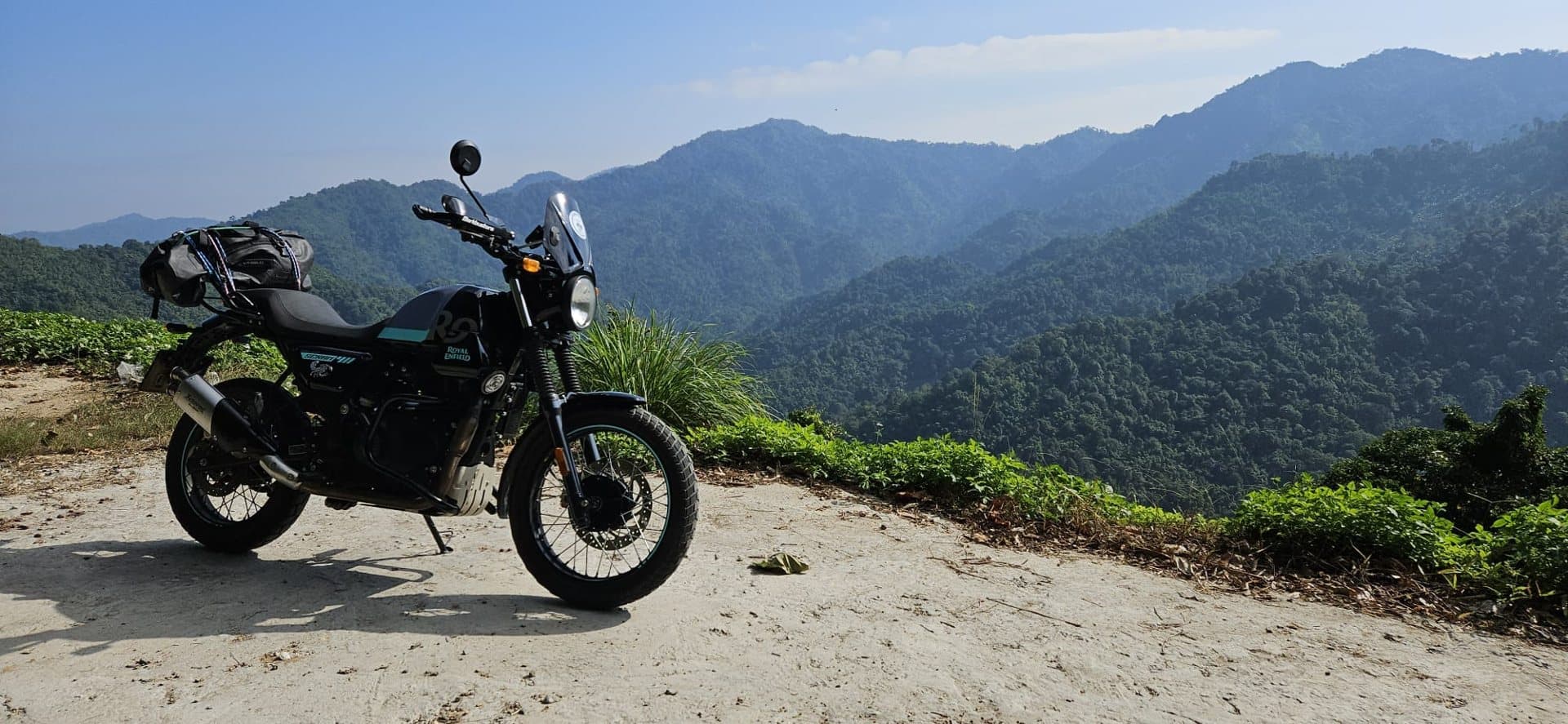 A Royal Enfield parked at a viewpoint over forested mountains